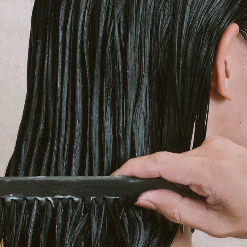 a woman is combing conditioner into her hair