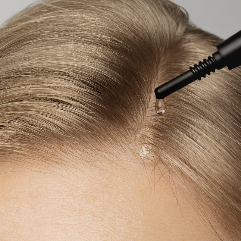 a woman applies serum onto her scalp