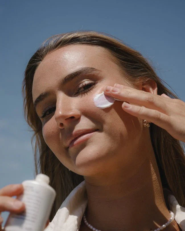 A woman applies sunscreen on her face